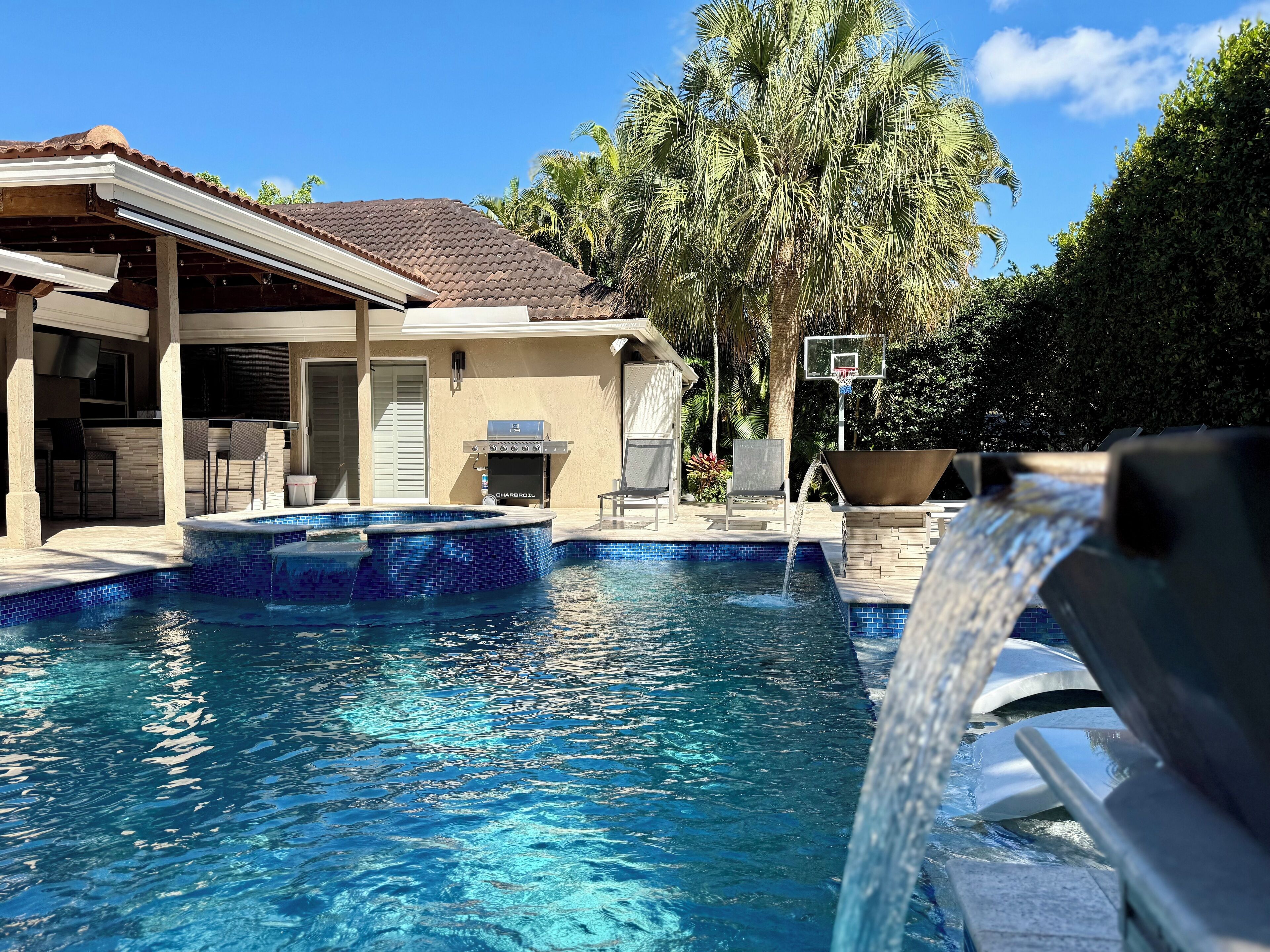 A swimming pool with a waterfall feature, a barbecue grill, and outdoor seating.