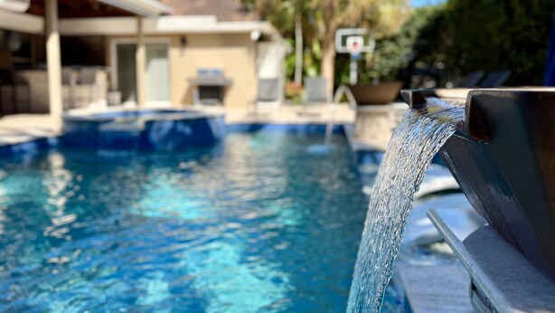 Una piscina amb una font, una zona coberta amb seients, i un cèrcol de bàsquet al fons.