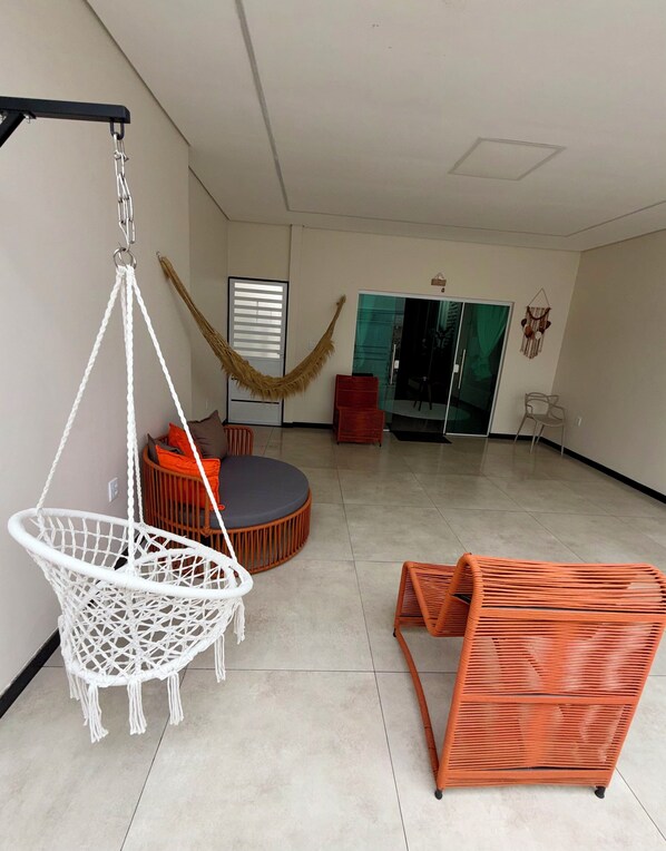 A spacious room with a hanging chair, a round seating area, and a glass door leading to another room.