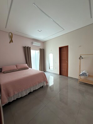 A bedroom with a bed, a wooden door, a window, and a wall-mounted air conditioner.