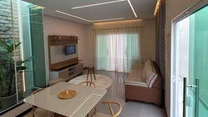 Een moderne woonkamer met een eettafel, stoelen, een bank, een televisie en een glazen scheidingswand.