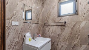 Un baño con paredes de mármol, un lavabo, un espejo y una ventana.