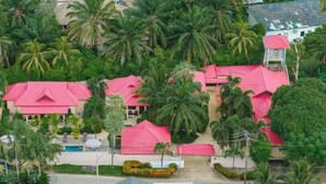 Un resort con varias construcciones, cada una con techo rojo, rodeado de exuberante vegetación y palmeras.