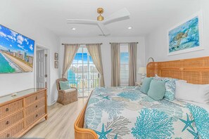 Un dormitorio con cama, cómoda de mimbre, ventilador de techo y una ventana grande con cortinas.