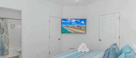 A bedroom with a bed, a ceiling fan, a TV on the wall, and a door leading to a bathroom.