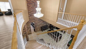 Ein mehrgeschossiges Interieur mit Treppe, einer Kristallleuchtre, Steinwand und einer Sitzecke.