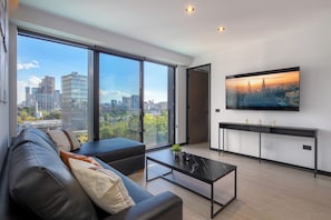 A modern living room with a large window, a black leather sofa, a coffee table, and a flat-screen TV mounted on the wall. - Elegant Modern Pool Gym Point Sâo Paulo-Andares (Guadalajara)