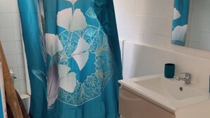 A bathroom with a shower curtain, a sink, a mirror, and a wooden bath mat. - Residence with sea view and close to beaches (Le Marin)
