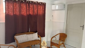 A room with a sofa, two chairs, a small table with decorative items, a woven rug, a door, and an air conditioning unit. - Residence with sea view and close to beaches (Le Marin)