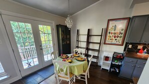 Ein Essbereich mit Tisch für vier Personen, einer Chandelieber und einer Küche mit Schränken sowie Wandkunst zum Thema Obst.