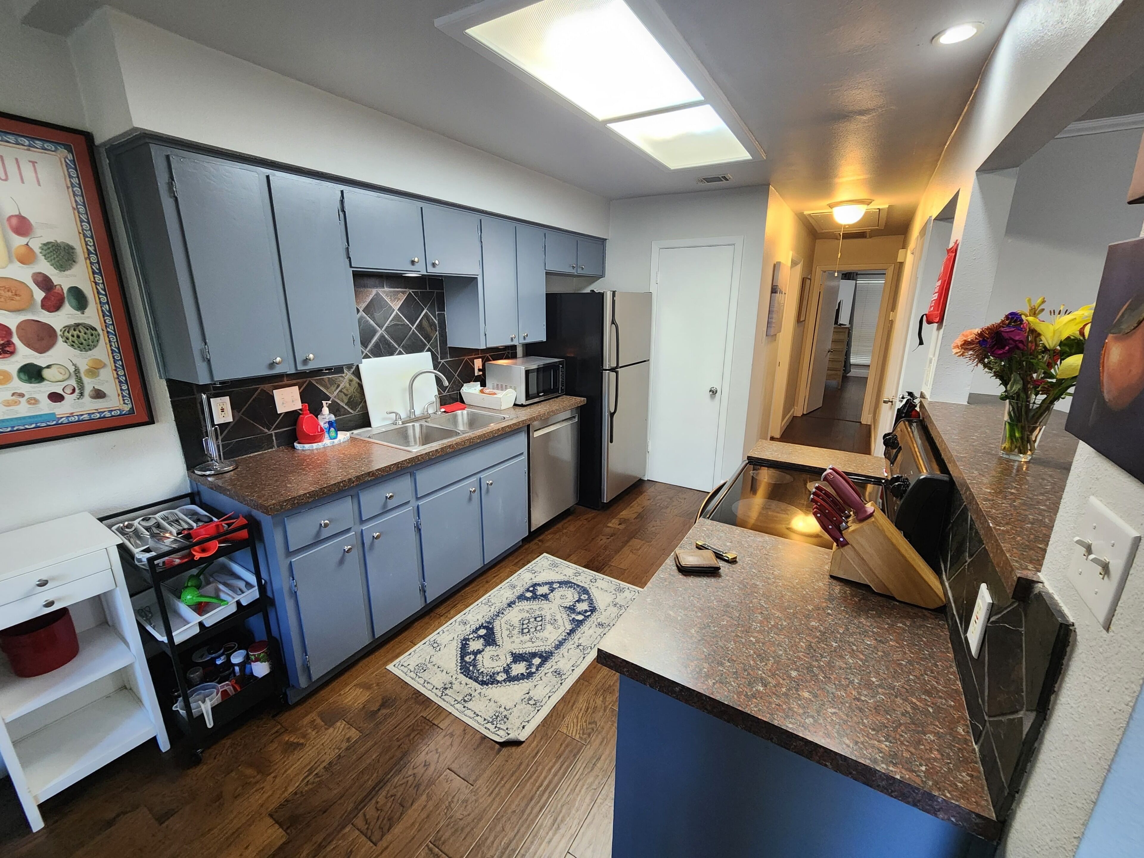 A modern kitchen with grey cabinets, a microwave, and a refrigerator. There is a rug on the floor and a vase with flowers on the counter.
