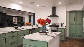 A modern kitchen with green cabinets, a central island, a stove, and a large window. - Private Pool • Movie Theater • Sleeps 12 / 4BR (San Antonio)