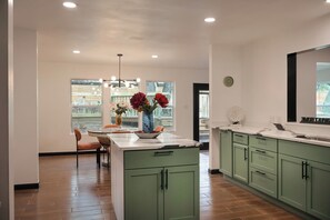 Une cuisine moderne avec des meubles de couleur verte, un îlot central agrémenté d’un vase de fleurs et un coin repas avec des chaises.