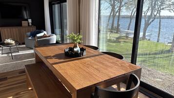 Un comedor moderno con una mesa de madera, sillas negras y vistas a un lago a través de amplios ventanales.