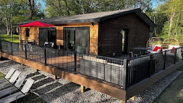 A modern cabin with a deck, outdoor seating, and a covered patio area.