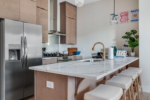 A modern kitchen with stainless steel appliances, a central island with stools, and a large window. - NEW!Pink Palace:Rooftop Hot Tub, Pool, Arcade, Beer Pong, Karaoke,BBQ, Game Room (nashville)
