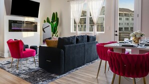 Ein modernes Wohnzimmer mit einem schwarzen Sofa, roten Sesseln, einem Flachbildfernseher, einem Kamin und einem großen Fenster mit durchsichtigen Vorhängen.