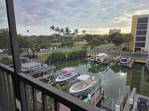 A marina with boats docked, a bridge, and a building in the background. - Relaxing Corner Condo on Canal - Casa Marina 2b/2b – Short Walk to the Beach! (Fort Myers Beach)