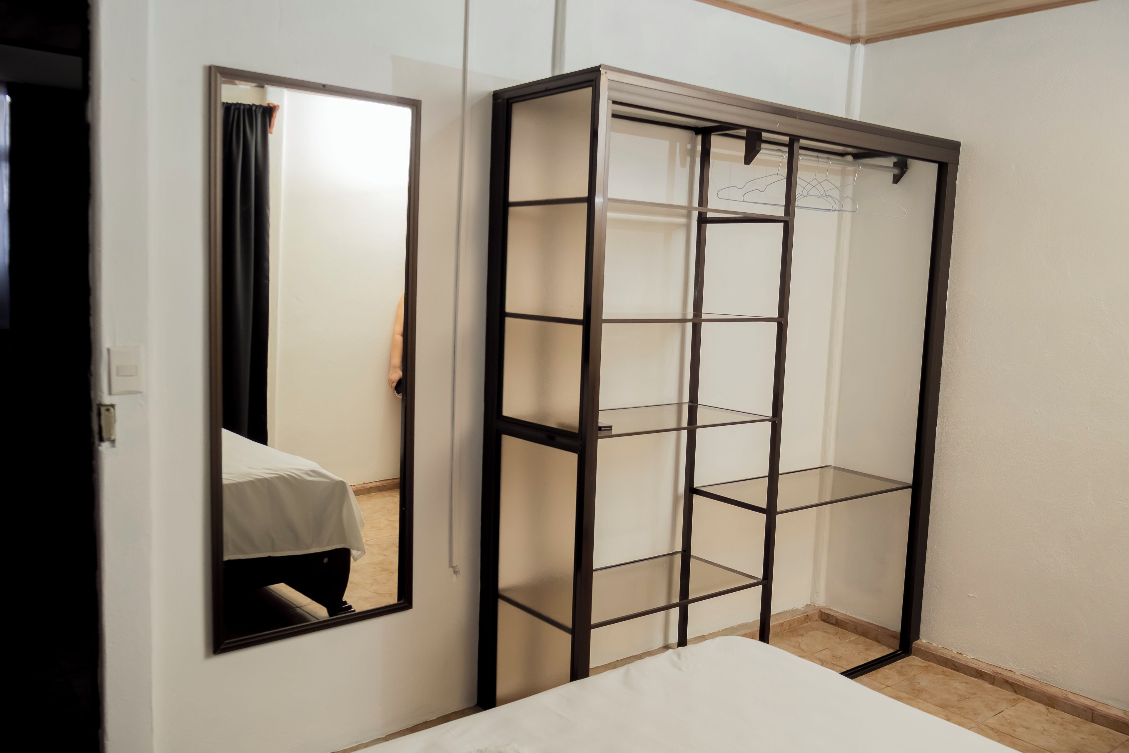 A room with a bed, a mirror, and a metal shelving unit.