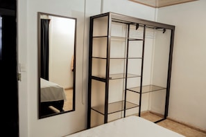 A room with a bed, a mirror, and a metal shelving unit.