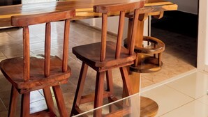 Un set di sgabelli in legno con un tavolo in legno, angolo cottura con fornello e una porta che conduce a una camera da letto.