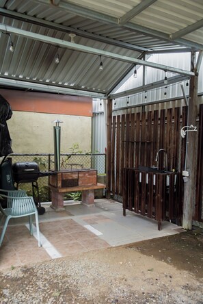 Un espace extérieur aménagé en patio, avec un barbecue, un banc et une structure de toit en métal.