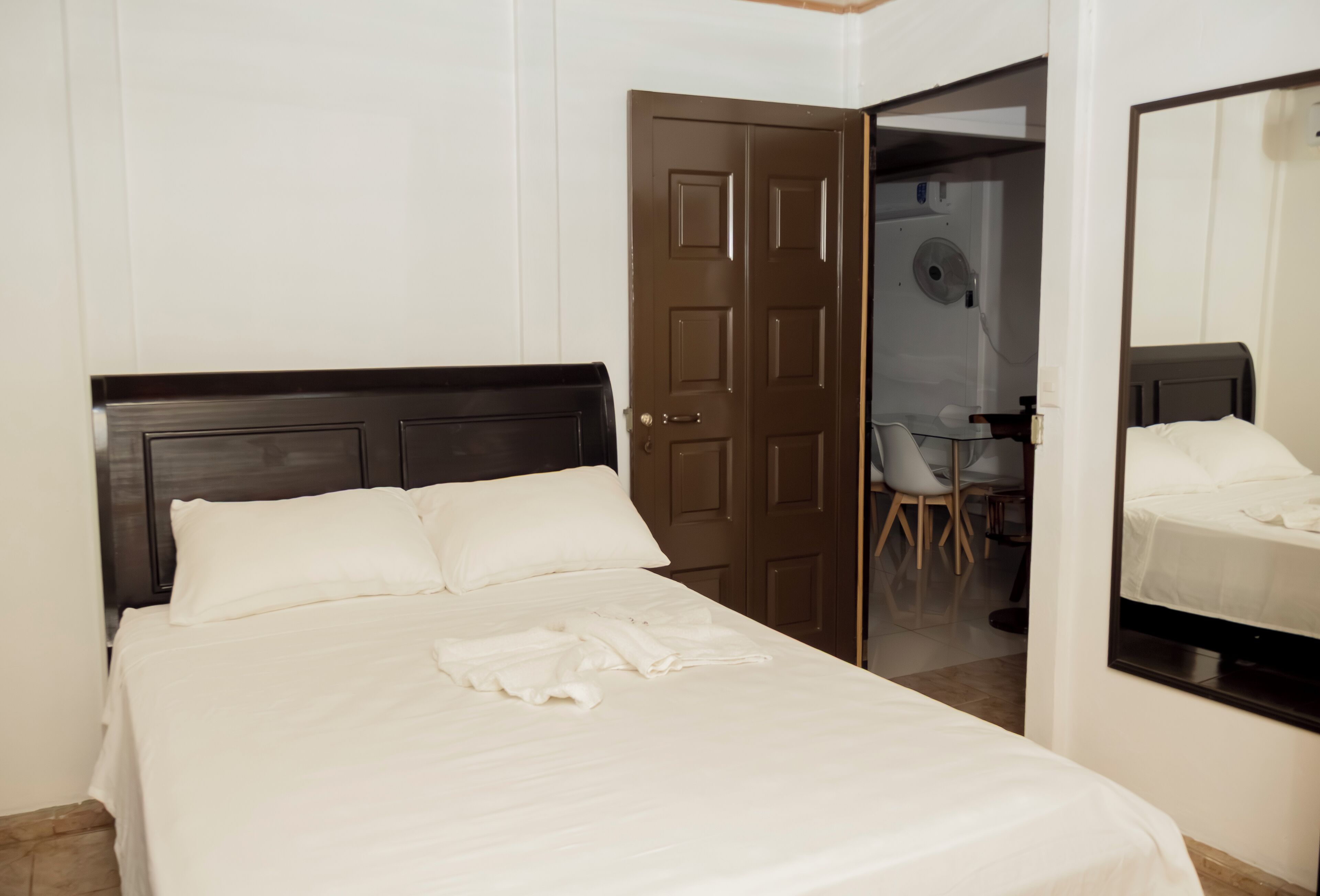 A neatly made bed with white linens, a dark wooden headboard, and a brown door leading to a bathroom.