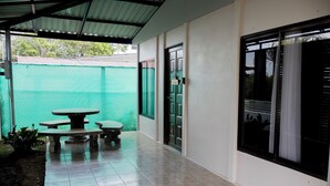 Un'area esterna coperta con tavolo e panche, una porta e una finestra con tende.