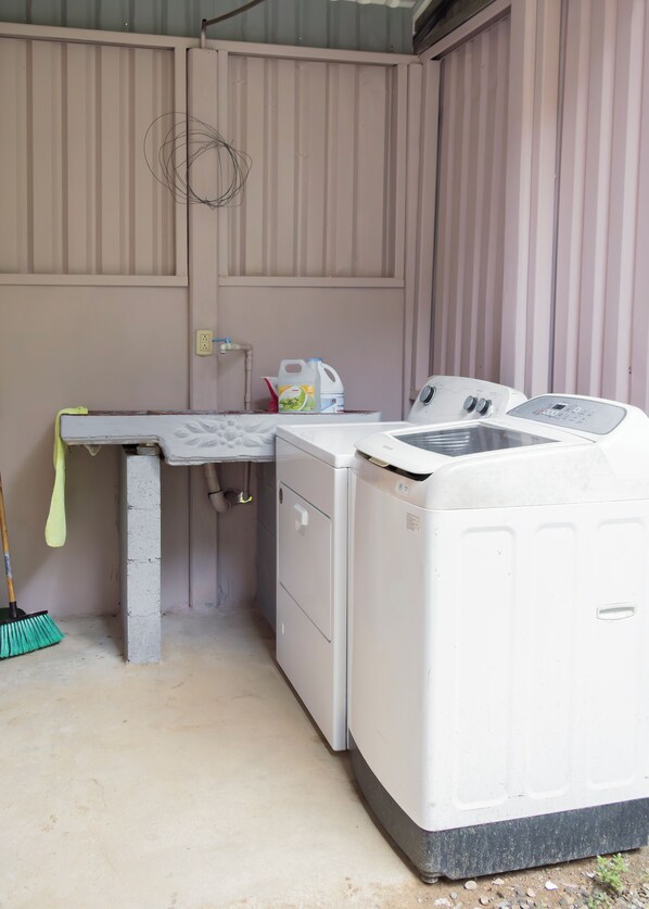 Un espace dédié à la lessive, comprenant un lave-linge, un étendoir, un balai et un pichet à lait.