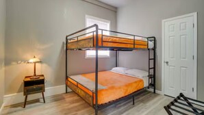 En køjeseng med en trætrap, et lille natbord med en lampe og en hvid dør.