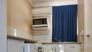 A compact kitchen with white cabinetry, a built-in oven, and a microwave. - Jefferys Motel (Kearneys Spring)