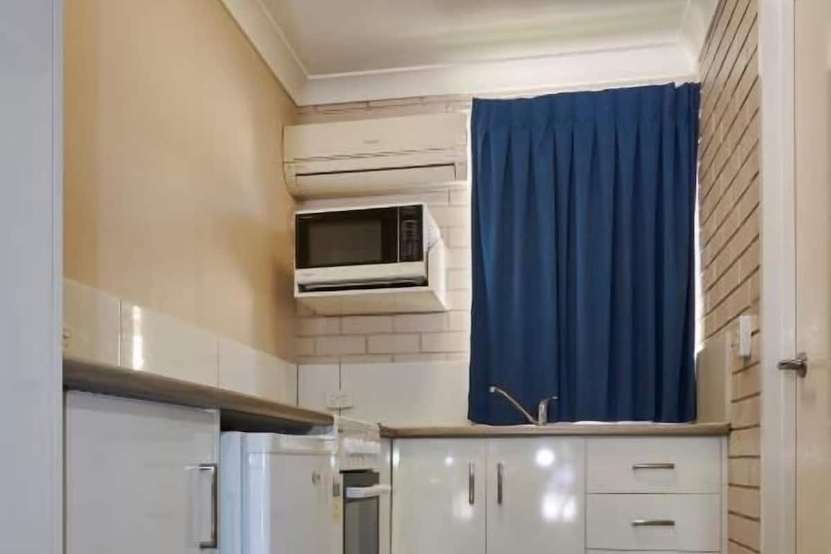 A compact kitchen with white cabinetry, a built-in oven, and a microwave.