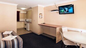 A compact hotel room with a kitchenette, a dining area, a TV mounted on the wall, and a bed with a striped blanket. - Jefferys Motel (Kearneys Spring)