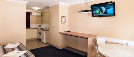 A compact hotel room with a kitchenette, a dining area, a TV mounted on the wall, and a bed with a striped blanket.