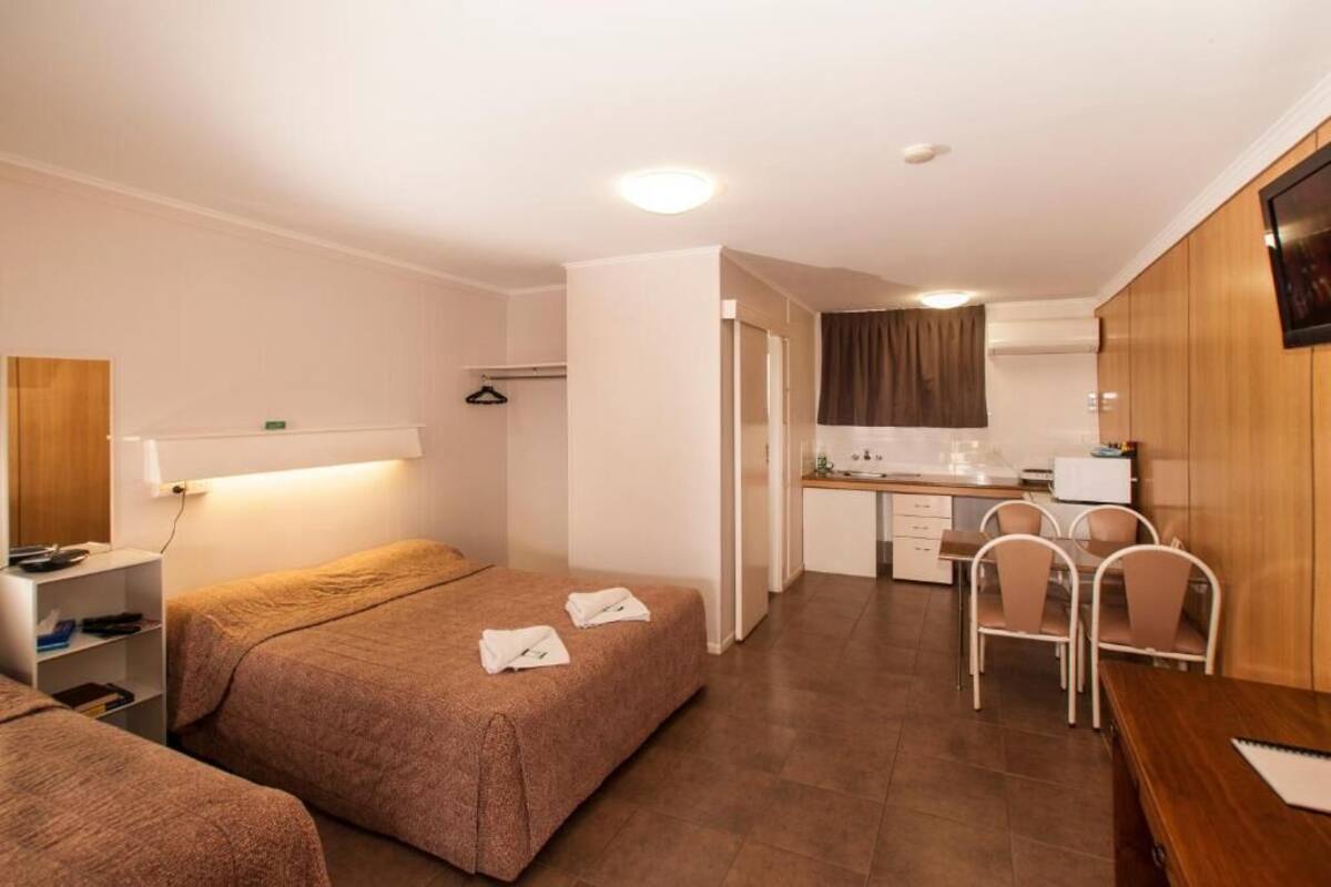 A hotel room with two beds, a kitchenette, a dining area, and a TV.