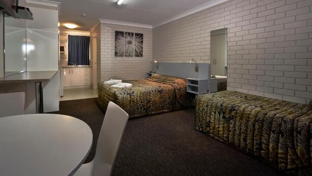 A compact hotel room with a bed, a desk, a chair, a mirror, and a wall-mounted artwork. - Jefferys Motel (Kearneys Spring)