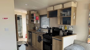 Een functionele keuken met een kookplaat, spoelbak en magnetron. Een zithoek met een bank en een salontafel.