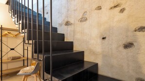 A modern staircase with black steps and metal railings, leading to a room with a concrete wall and a wooden chair. - Al Vignale - La Vista by Interhome (Valtellina)