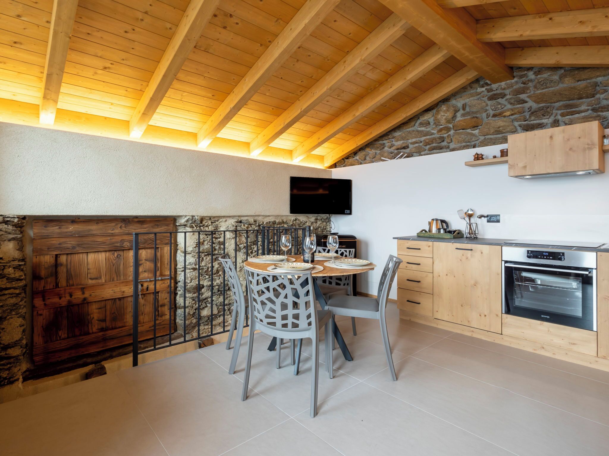 Una cucina con travi in legno, parete in pietra e televisore montato sopra il bancone.