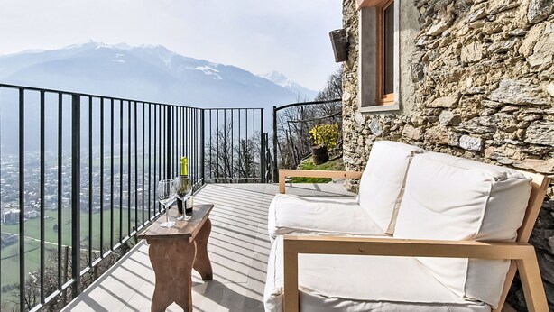 Un balcón con una mesa de madera, un sofá blanco y vistas a las montañas.