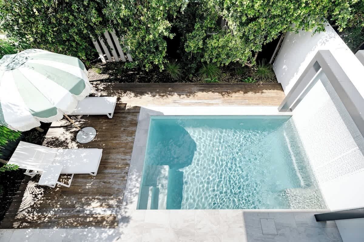 Ein rechteckiger Swimmingpool mit klarem Wasser, umgeben von einer Holzterrasse und weißen Liegestühlen.