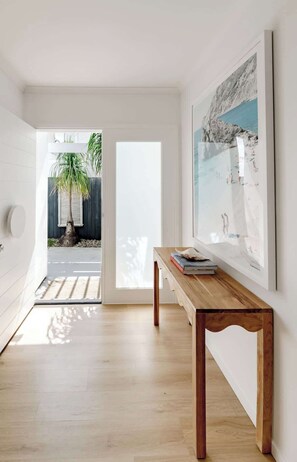 A modern interior with a wooden table, a framed artwork, and a view of a tropical outdoor area. - Sunny Gem on Sunrise - steps to the beach! (Sunrise Beach)