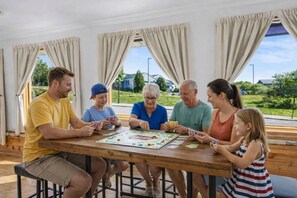 A family playing a board game at a wooden table with large windows and curtains. - Walkable Egg Harbor Retreat with Water Views (Egg Harbor)