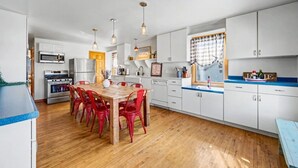 Une cuisine moderne avec une table à manger, des chaises rouges, des meubles blancs et un plan de travail bleu.