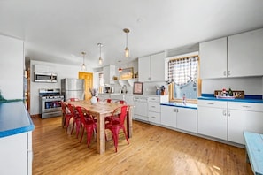 A modern kitchen with a dining table, red chairs, white cabinets, and a blue countertop. - Walkable Egg Harbor Retreat with Water Views (Egg Harbor)