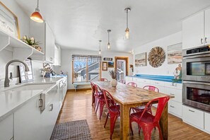 A modern kitchen with white cabinets, a wooden dining table, red chairs, and pendant lights. - Walkable Egg Harbor Retreat with Water Views (Egg Harbor)