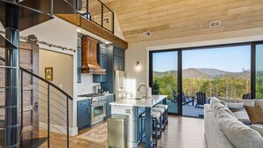 Une cuisine moderne dotée d’un îlot central, d’un coin repas offrant une vue agréable et d’un escalier menant à un étage supérieur.