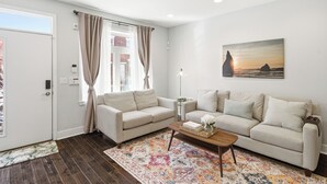 Ein Wohnzimmer mit zwei Sofas, einem Couchtisch, einem gemusterten Teppich, einem Gemälde und einer Tür mit Vorhängen.