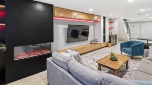 Ein modernes Wohnzimmer mit Flachbildfernseher, Kamin, Sofa, Couchtisch und einem blauen Sessel.