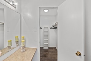 Un couloir étroit avec un miroir, une porte blanche, un plancher en bois et une armoire blanche avec une échelle.